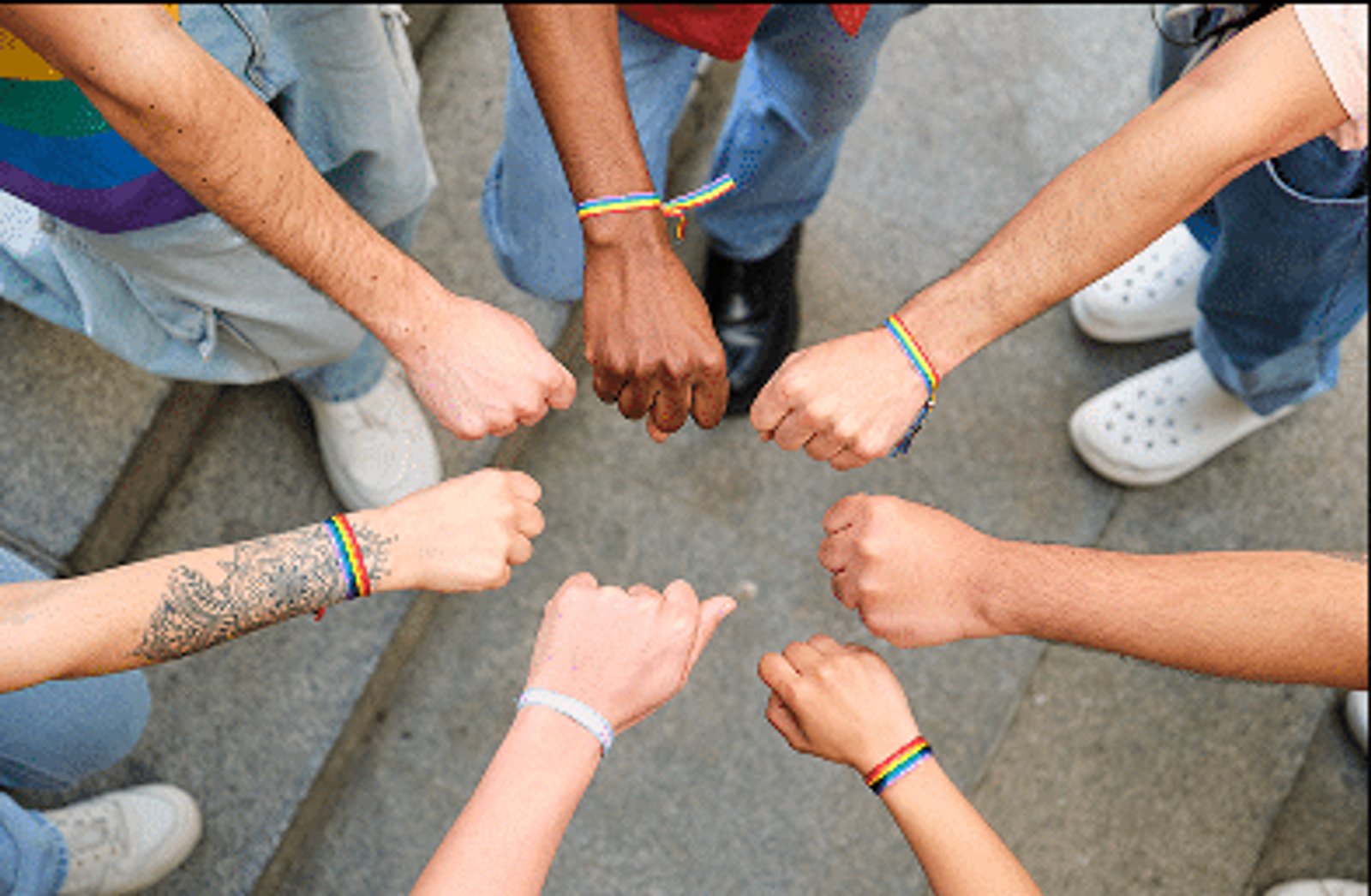 A circle of people's hands in fists for solidarity, wearing pride bands
