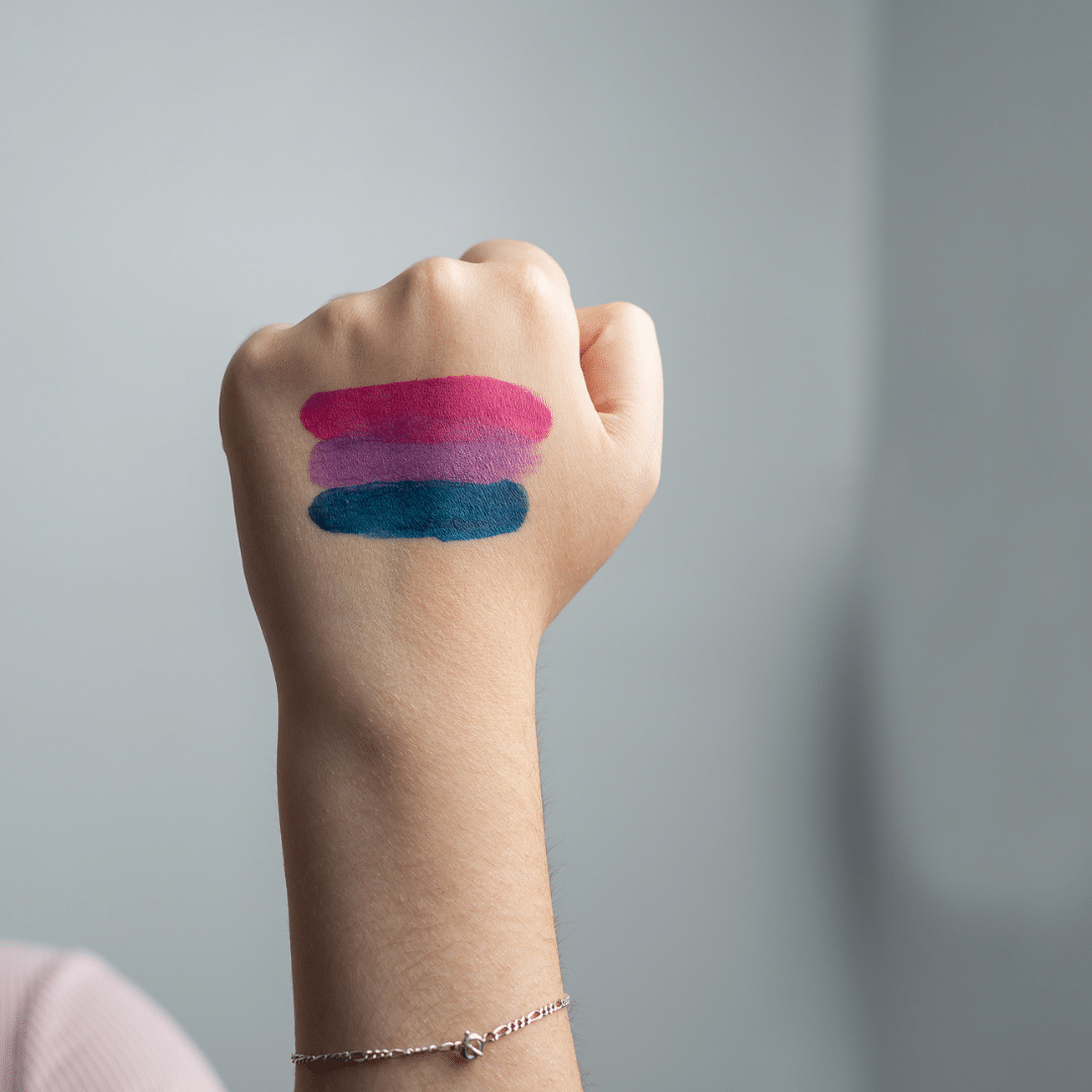 A raised fist painted with the pink, purple, and blue stripes of the bisexual pride flag