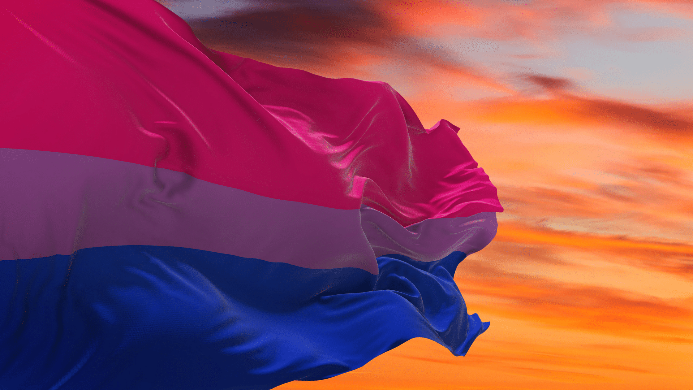 A bisexual pride flag billowing against a vivid orange sunset sky