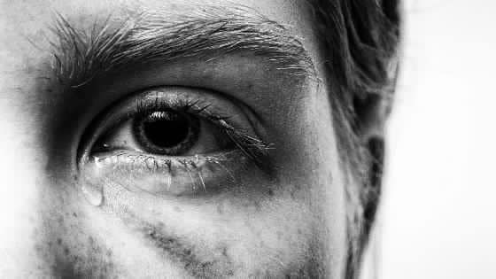 A close-up of a tear rolling down from one eye in a black-and-white portrait