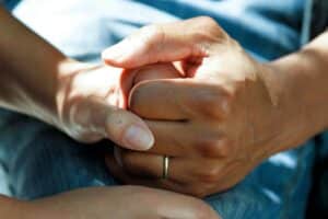 Two people holding hands closely, with one hand wearing a ring